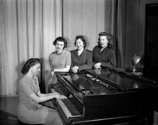 University of Wisconsin Dames Club Music Group Four of the leaders of the music section of the University of Wisconsin Dames club gathered around a piano.
From left to right: Mrs. Carlton R.(Florence) Sell, 751 Jenifer St.; Mrs. Joseph (Maxine) Bednarski, 919 W. Dayton St., co-chairman of the music group; Mrs. Ralph (Lillian) Smuckler, 317 State St., chairman; and Mrs. Theodore (Ruth) Toebaas, 336 Norris Ct.