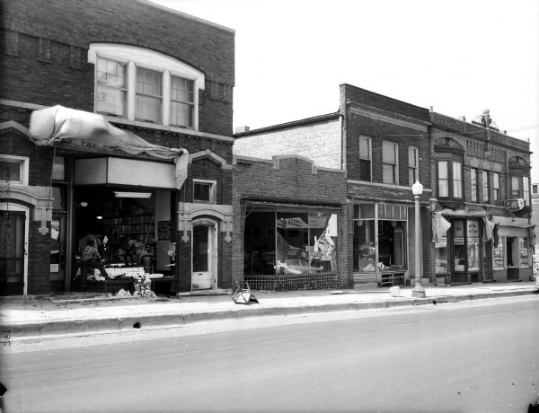 View down East Wilson Street where the plate glass windows of three storefronts were shattered during a high wind storm that hit Madison. The three stores, left to right, are The Factory Outlet Store, 308 East Wilson; Volunteers of America, used furniture store, 310 East Wilson; and their used clothing store next door at 312 East Wilson. Also pictured is Guerein's Cafe, 316 East Wilson.