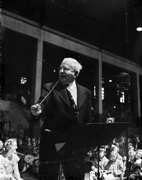 Professor E.B. Gordon conducts at the seventeenth annual radio music festival. Professor Gordon has a radio class of 90,000 boys and girls who are enrolled in Gorden's "Journeys in Music Land" course on the State Radio Council's network of stations.