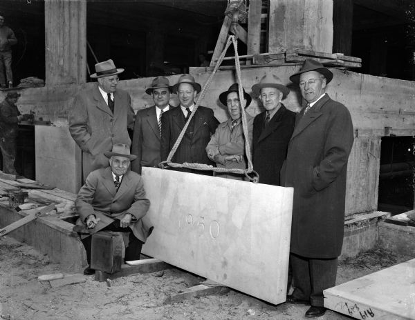 The cornerstone for the million-dollar four-story addition to the Madison Vocational School was laid at the corner of North Carroll and West Dayton Streets corner of the structure. Emil J. Frautschi, president of the Madison Vocational and Adult Education board, wielded the trowel at the ceremonies. Standing behind Frautschi and the cornerstone are, left to right, Richard W. Bardwell, director of the Vocational school, George J. Forster, acting city manager, Fred M. Mason, member of the vocational education board, John P. Butler, supervisor of the building project, Frank G. Collester, board member and Mark A. Cullen, president of J. P. Cullen and Sons, general contractors for the job.