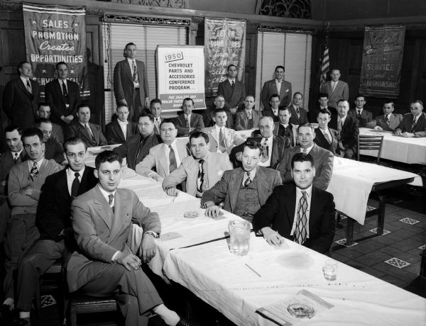 Group portrait of men dressed in business suits at a Chevrolet sales meeting.