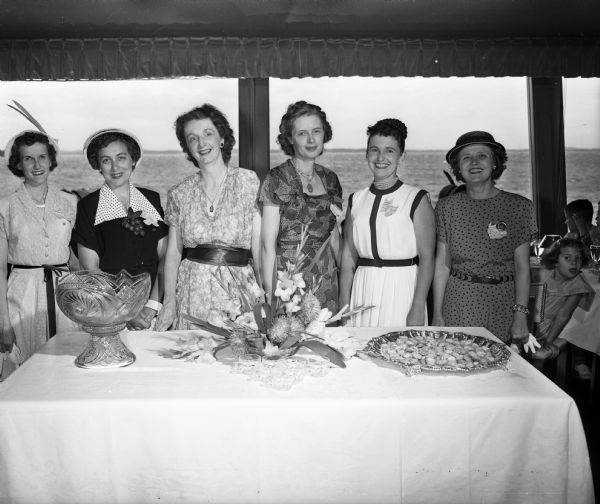 Six sorority alumnae who were hostesses for the marionette party at the Edgewater Hotel pose for a portrait around a banquet table. Left to right are: Mrs. James White, Mrs. Hollis Toynton, Mrs. Richard C. Church, Mrs. Carl Engler, Mrs. Charles Vaughn, and Mrs. Carl Anderson.