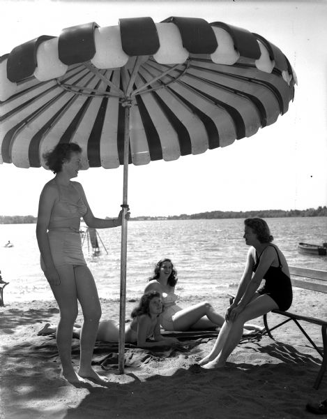 Beach scene at Lake Ripley showing three young women under an umbrella.