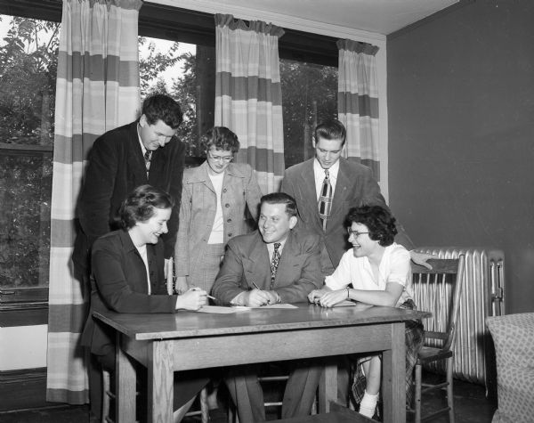 Staff members of the Neighborhood House, 768 West Washington Avenue, pose around a table for a group portrait. Seated, left to right: Louise Schleicher, assistant program director; Al Waxman, director; and Shirley Witkin, secretary. Standing: Bob Rowen, incoming director of the future South Madison Neighborhood House; Lois McConnell, U.W. graduate student; and Royal Thomas, U.W. graduate student.