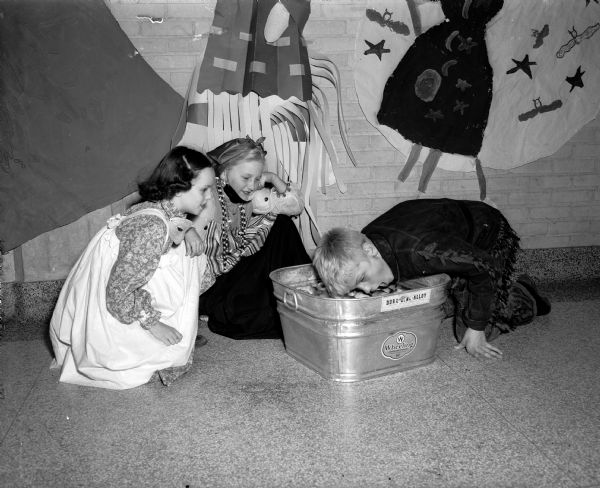 At Lapham School, more than 800 costumed children and their parents attended one of the largest Halloween night parties held in Madison. A boy is shown bobbing for apples as two girls are watching.