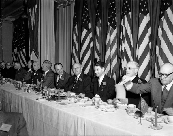 Men sitting at the speakers' table at the Madison and Wisconsin Foundation annual banquet with state, city and university officials as invited guests. Included are: Col. Collins H. Ferris, Commandant of the 128th Fighter Interceptor Wing at Truax Field; Acting City Manager, George Forster; Acting City Manager; Major General Ralph J.  Olson, State Adjutant General; Assemblyman Ora. R. Rice; Assembly Speaker Governor Walter Kohler, Jr.; F. Halsey Kraege, Foundation President; and Lieutenant Governor, George M. Smith.