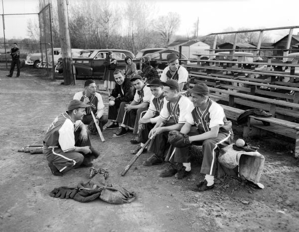 Members of the Board of Realtors softball team gather around the bleachers during their opening game of the 1951 Madison softball season at Franklin Field. Around the semi-circle from left to right are: Bob Paul, Doug Schmale, Will Vanderhoft, Warner Schorr, Ed Tallard, Manager Archie Paulson, and Bill Schmale. Sitting behind the group is Jim Parr(?).