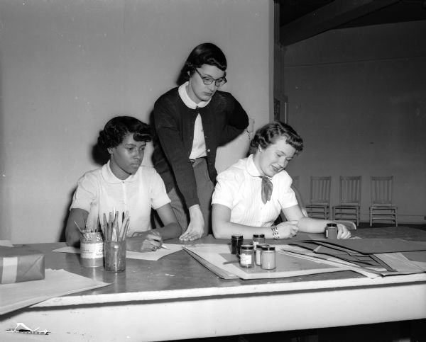Madison YWCA Y-Teens Beverly Hill, left, and Carol Sterling make posters for the Y-Teen open house and style show at the YWCA. Mary Ellen Kruger, standing, the Y-Teen adviser, is shown inspecting the girls' artistic efforts.