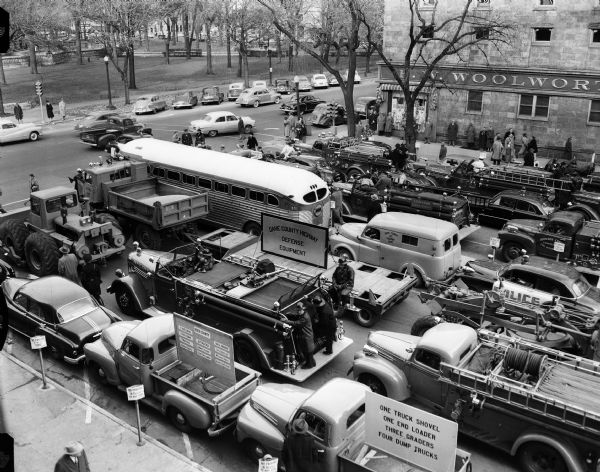 Mobile Civil Defense Test Elevated view of some of the 125 vehicles which were used in Wisconsin's first civil defense support battalion test in Madison. The vehicles are parked on Monona Avenue in front of the Wisconsin State Capitol. The F.W. Woolworth Company store can be seen on the Main Street corner.