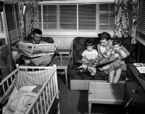 The Larson family, including a mother, father, and two children, are sitting in the living room of their mobile home (probably at Truax Field trailer camp). "Residents of the Truax Field trailer camp will petition the city council and Mayor George Forster to hold off impending eviction notices until May." WSJ 11-21-1951. The land is needed by the air force. The Madison Housing Authority manages the trailer park for the city.