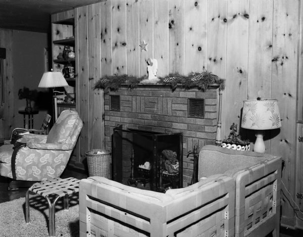 Interior view of the recreation room in the house of Harold Baumgartner at 240 South Oak Street, featuring pine paneling on the walls, a brick fireplace and comfortable furnishings.