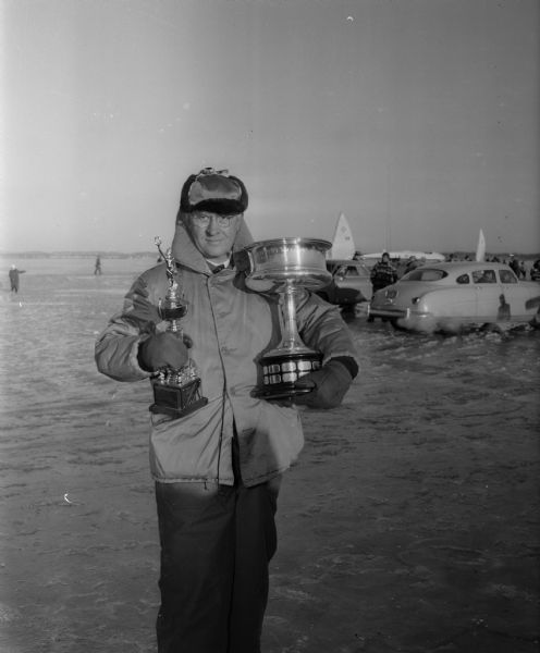 Orvin T. Havey is shown with trophies for his iceboat, the "Mary B," that won the Class A Championship in the Northwestern Ice Yachting Association ice regatta on Lake Monona. In his left arm is the traveling trophy and in his right arm is the trophy he gets to keep.