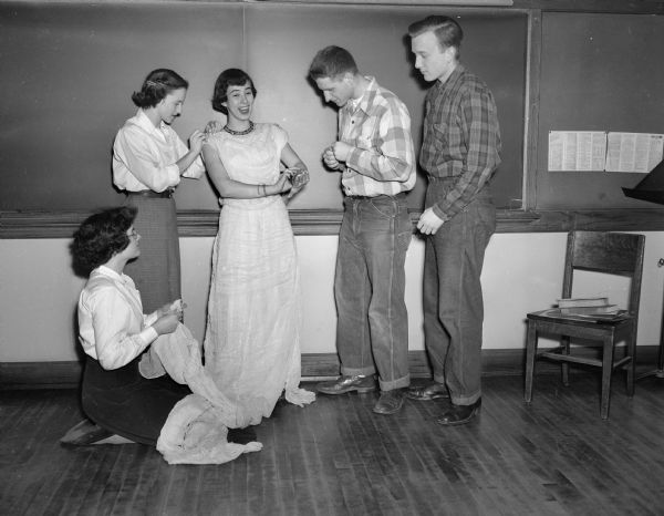 Pat McGrath, standing at left, a member of the costume crew for the West High school play "Stardust," is shown fitting a gown on Judy Hicks, center, as Irvin Rosenberg and Henry Goehring, at right, watch the procedure. Seated is Lorna Jean Steul, also a member of the costume crew.