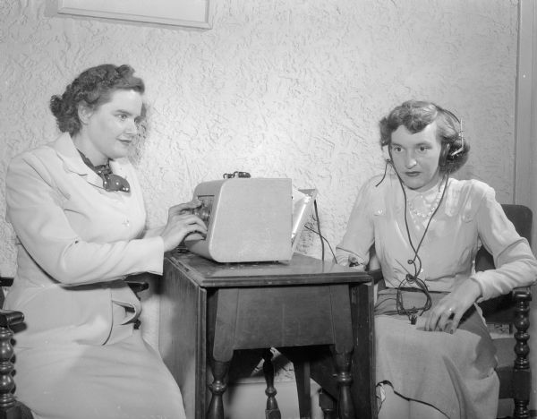 "With her roommate Helen Blohm (right) playing the role of the subject, Mary Louise Lane (left) checks her hearing with an audiometer. Miss Lane, blind co-ed who is working for her doctor's degree in speech, 'reads' the instrument on a specially-constructed dial." P.B. Grove of the Grove Hearing Aid service, Madison, modified the audiometer. He added a sound signal to replace hand signals and a Braille dial for Miss Lane.