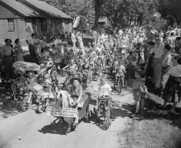 Some of the 300 children who took part in the Westmorland Fourth of July Parade line up on a narrow tree-lined Westmorland Boulevard. 3,000 people took part in the day's events. A child on a wagon decorated like a horse has a sign in the front that reads: "What Happened to those Open Spaces in Westmorland."