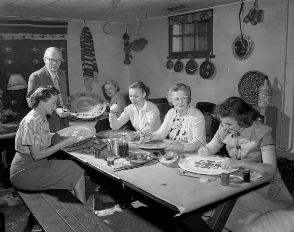 Members of the rosemaling class of the Shorewood Hills Community League sitting around a table. Shown are Karl K. Reese, the instructor, and Beatrice Cartwright, Patricia McGovern, Claire Dittmar, and Martha Olafsson. The group met for 10 weeks in the recreation room at the home of Grace Howdle on Crestwood Drive.