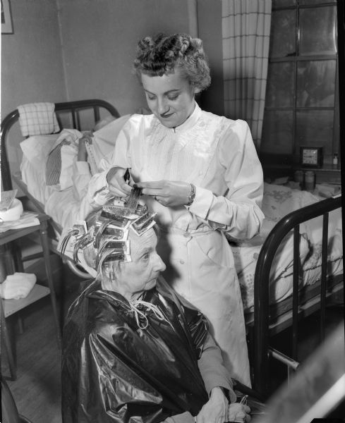 A resident of the Oakwood Lutheran Nursing Home is given a permanent by an apprentice in the Madison Vocational and Adult School cosmetology program.