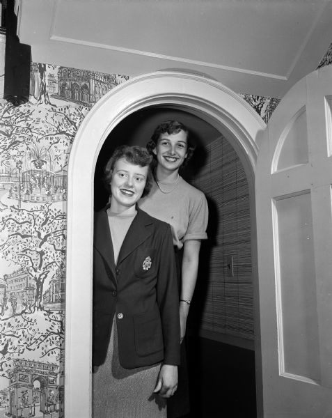 Portrait of two University of Wisconsin co-eds recently pledged to Alpha Chi Omega sorority. Standing in the arched doorway of the sorority house at 152 Langdon Street are Grace Jostad, left, and Susan Ohlis, right.