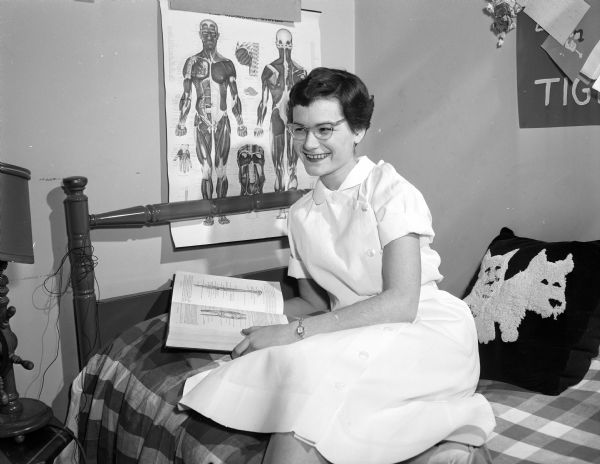 Margaret Fliegel holds a book while sitting on her bed in front of an anatomy chart.  She was a senior physical therapy student and a Easter Seal grant recipient.