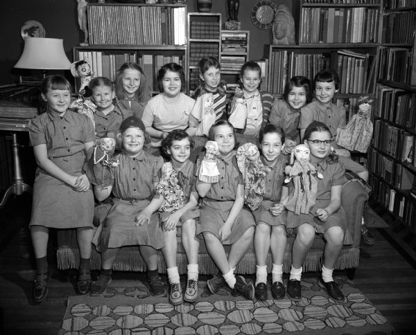 Portrait of 13 members of the fourth grade Brownie Troop of Lincoln School. They are shown with some puppets which they used in their program in honor of the 42nd birthday of the Girl Scout organization.