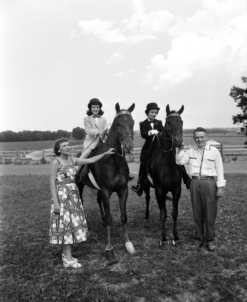 Portrait of Mr. and Mrs Ralph D. (Jennelyn) Timmons of 938 Waban Hill with their 2 daughters, Bonnie (left), 12, and Nancy, 19, seated on two horses.