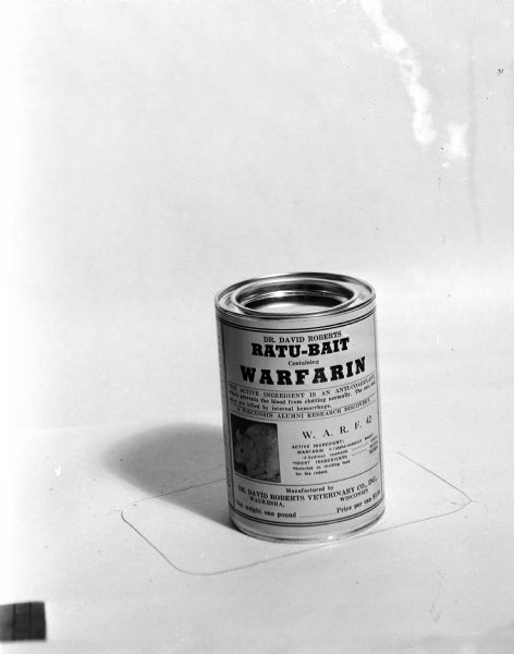 Studio photograph of a one-pound can of Dr. David Roberts Ratu-Bait containing Warfarin. The active ingredient is an anti-coagulate which prevents a block from clotting normally, resulting in the rats and mice being killed by internal hemorrhage. The product was a Wisconsin Alumni Research discovery.