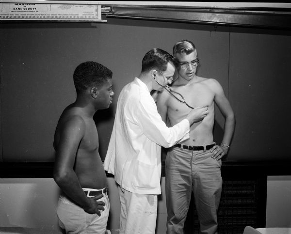 Ed Wing, Central High School football player, having his heart checked by Dr. Hubert Hamel. Al Smith, another Central High player, is looking on.