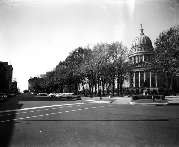 View of the East Main Street side of Capitol Park, one of four images making up a panorama of the southeast side of the Capitol Square, showing the Wisconsin State Capitol Building and Hegg statue.