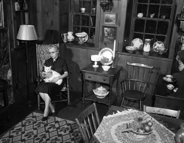 Slightly elevated view of Lenore Middleton (Mrs. Forest Middleton) posing with her cat in the antique-filled living room of her home at 3241 Highbury Road (address in 1955). The home was built in 1853 by Joseph Statz and is to be featured on the second annual house tour of the League of Women Voters in cooperation with the Madison Chapter of the Wisconsin Division of Architects.