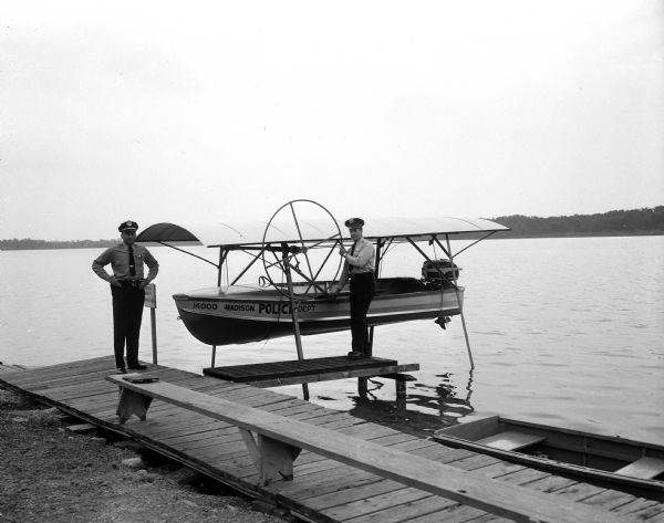 New Madison police rescue boat, in operation on Lake Wingra, is shown in its boat lift at Knickerbocker Street boat livery. Sgt. Robert Ferris (left) and Patrolman Gordon Erickson demonstrate the hoist.