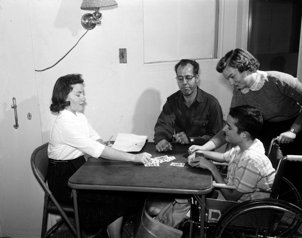 Methodist hospital student nurses Karolyn McCauley (left) and Mary Bach (right) join in a card game with Robert Lloyd of Janesville and Jack Durham (in a wheelchair) from Tazewell, Virginia, at the Wisconsin Neurological Foundation. They are taking part in a state-wide project at various hospitals and welfare centers as part of Student Nurse Week.