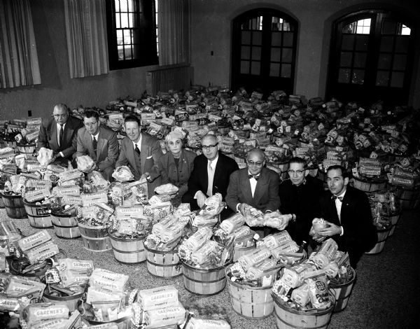 Members of the Salvation Army board posing amidst the Christmas food baskets assembled by the Salvation Army. Left to right are: Alan Hackworthy, Lyle Andrews, Whitford Huff, Geneva Schoenfeld, Walter Rhodes, Emanuel Simon, Major Lloyd Robb, Milwaukee, and Feilx Kremer.