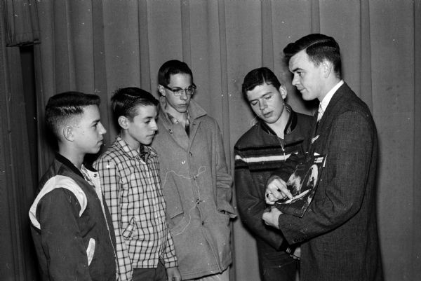 Four Madison Newspapers, Inc., carrier salesmen (or newspaper home delivery boys) and district circulation manager, Clinton Vandall (right) are shown looking over possible awards for new subscriptions, such as prizes, cash, or trips to Chicago. The boys are Bill Cox, Tom and Marden Junck, and John Padrutt.