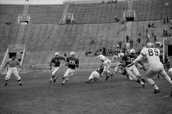 Alumni-Varsity Football Game Action shot during the annual University of Wisconsin Alumni-Varsity football game at Camp Randall Stadium. Madison West's Jim Bakken (28) sweeps right end while Bob Zeman (34) trails and Tony Anthony (36) cuts to block alumni player Dave Kocourek (89).