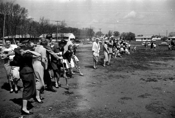 More than twelve people in their Sunday clothes gathering in an open lot at Gilbert Road and Tolman Terrace to note the start of construction of their church building.