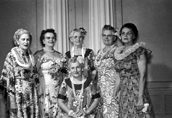 Six women dressed in Hawaiian muu-muus gather for the spring luncheon of the Daughters of the Nile. Seated is Mrs. Thomas Pleuss of Edgerton. Standing, left to right, are Mrs. Erma Smith, Mrs. Carolyn Emerson, Mrs. Mayme Peterson, Mrs. Helen Moore, and Mrs. Rudy Lindberg of Edgerton.
