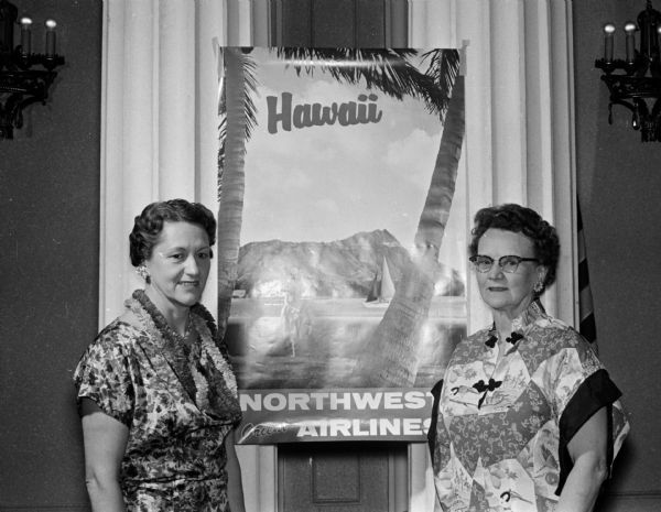 Mrs. Minnie Judd (left) and Mrs. Nora Rorge stand by a Hawaiian poster at the spring luncheon of the Daughters of the Nile.
