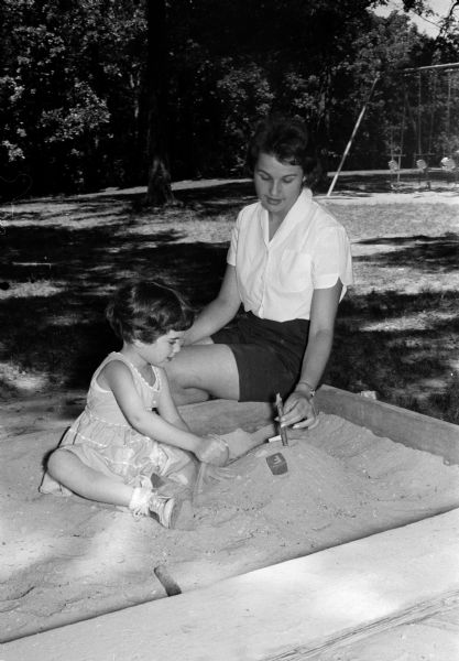 Mary Gandt sits with her young charge, Dana Rosenthal, in the sandbox. Mary is babysitting to earn money for the Girl Scout trip to a Round-Up in Colorado.