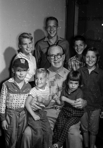A group of kids is shown with "Roundy" Coughlin. They put on a carnival in the back yard of Jim Riphahn on Madison's east side to raise money for "Roundy's Fun Fund" for underprivileged boys and girls. They are, front row, left to right: Doug Preez, Jeffrey Morgan, "Roundy," Kathy Morgan, Sue Preez; second row: Carol Fell, John Riphahn, Tom Riphahn.