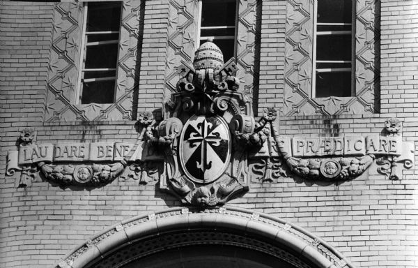 Inscription in relief above the arched doorway that is the main entrance to Edgewood High School. The inscription reads "Laudare, Benedicere, Praedicare," which means "to preach, to bless, to pray" and is the motto of the order of St. Dominic. Architect Albert Kelsey, grandson of Governor Cadwallader C. Washburn, designed the building which is a cream color with black and white trim to represent he habit of the Dominican nun.