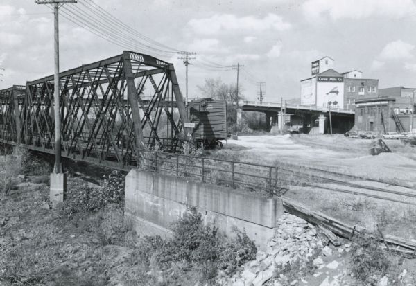 View looking north under Wausau's Scott Street (also State Highway H 29 and Business 51) Bridge, with a railroad bridge in the foreground and the warehouse of the Cereal Mills Company.
