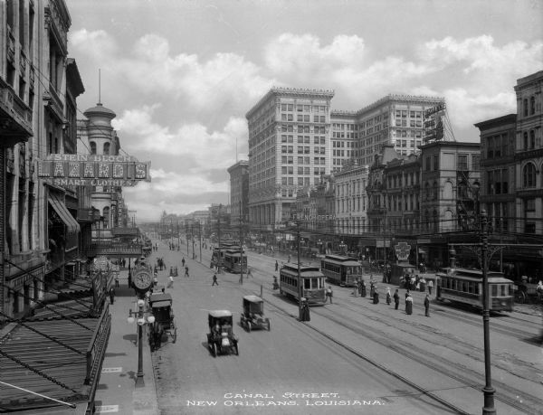 Elevated view of Canal Street scene. Automobiles, streetcars and pedestrians are moving along the busy street. Store sign reads: "Stein-Block LAZARD'S Smart Clothes." Caption reads: "Canal Street, New Orleans, Louisiana."