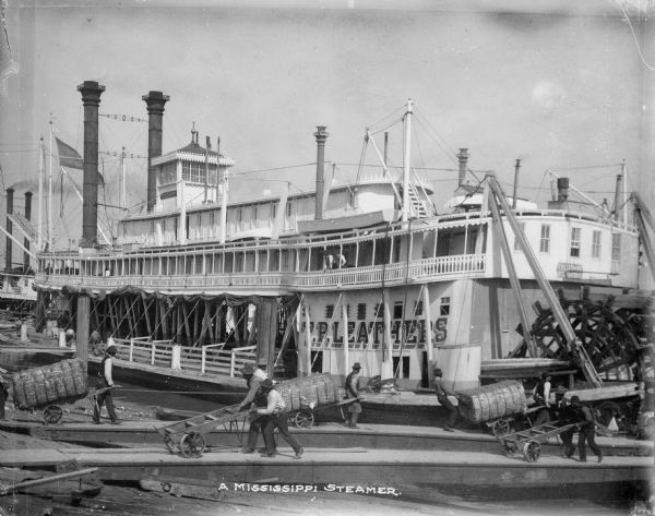 View of the T.P. Leathers Steamer at dock. Men can be seen loading cargo onto the ship. Caption reads: "A Mississippi Steamer."