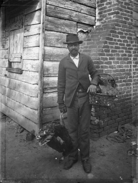 A man poses while selling chickens on the street. A building with an exterior brick chimney is behind him.