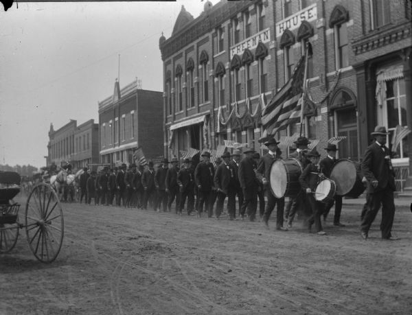 Grand Army of the Republic in Memorial Day Parade, in front of the Freeman House. Leading the ranks is probably James Livingston, Alvin "Bean" Hagen is probably playing the snare drum, and Henry Moldenhauer is the taller boy playing the bass drum.