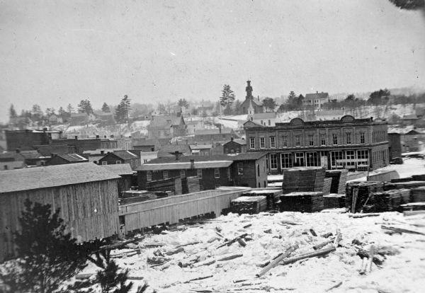 Town and business district, showing the early covered bridge across from the tail race of the powerhouse, with logs overflowing the river into yards, probably during the Ice Gorge of 1876.