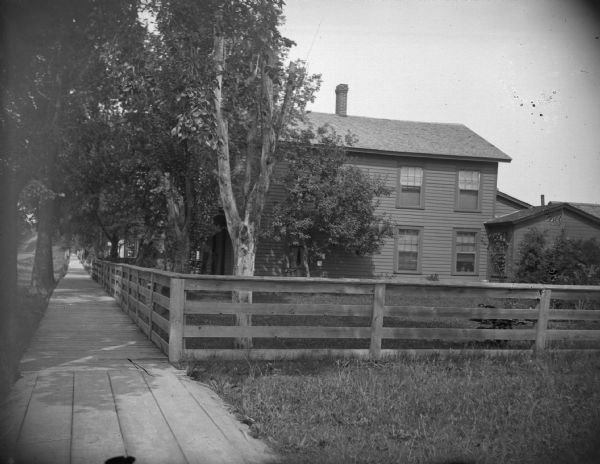 Two-Story Clapboard House Two-story clapboard house in town with a fenced yard and board sidewalk,