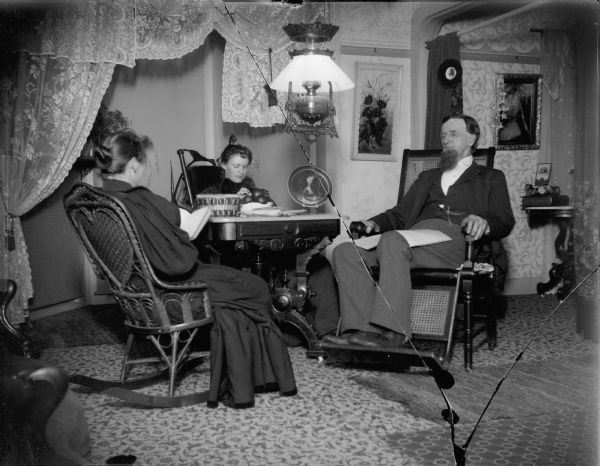 Amos Elliot, pioneer stage coach driver, enjoying a quiet evening at home with his second wife, and her daughter (center), Stella Hart.