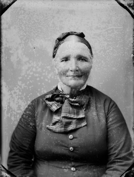 Studio portrait of a seated elderly woman wearing a head scarf and a large plaid necktie.