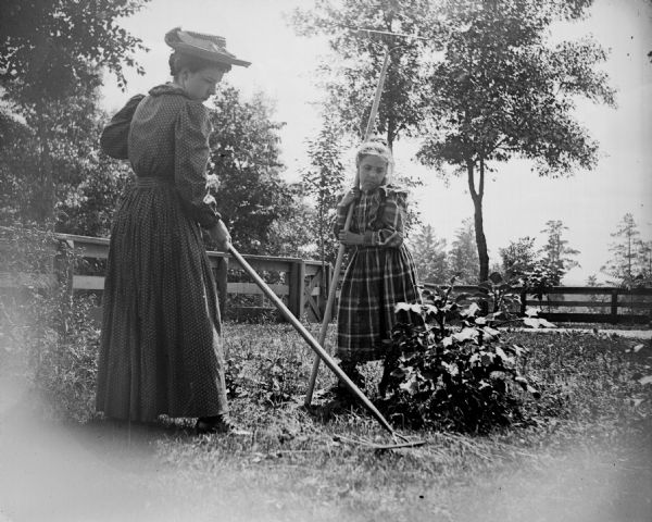 Woman in hat and young girl raking the lawn.